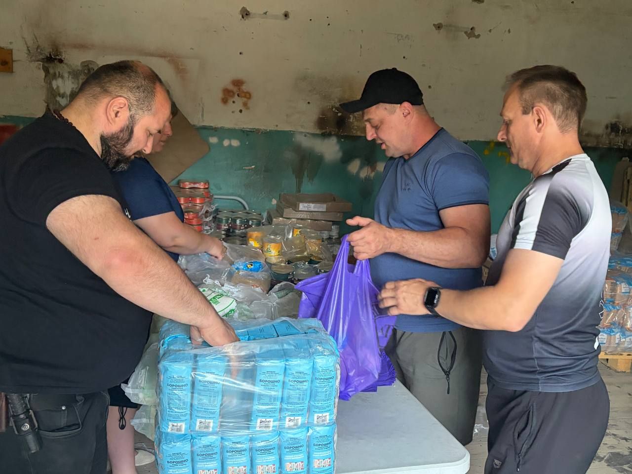 Четверо людей з команди фасують продукти у фіолетові пакети за столом на складі