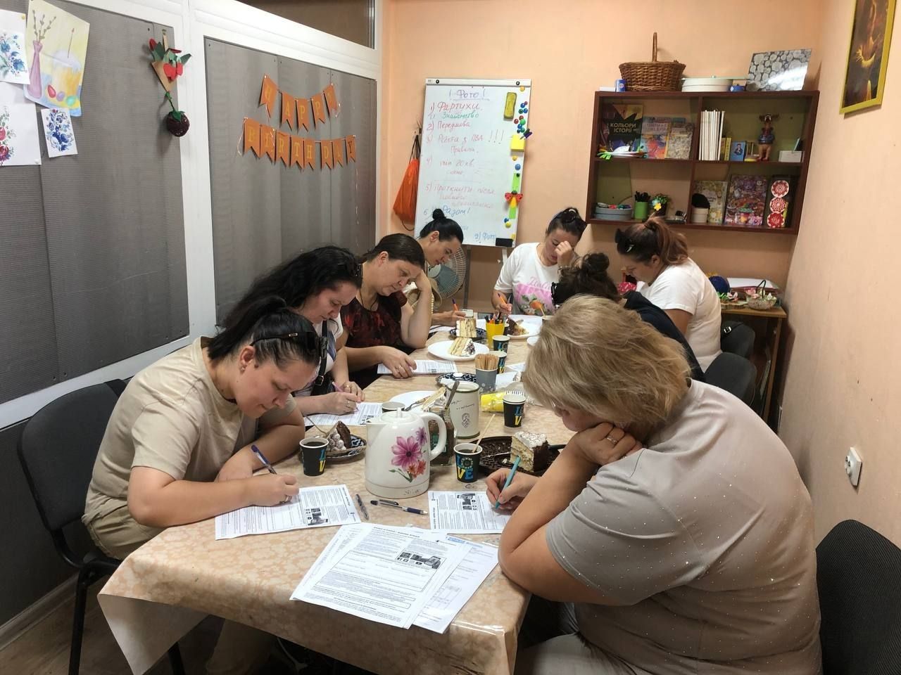 Руки батьків заповнюють завдання на аркушах за столом, поруч чашки і чайник