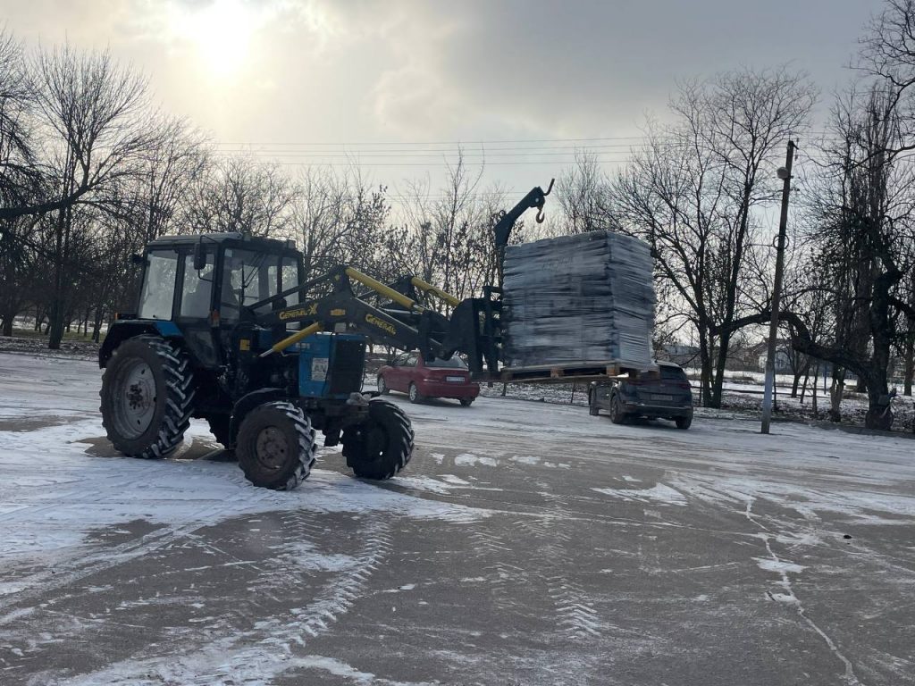 Трактор перевозить паливні брикети на причепі засніженою дорогою