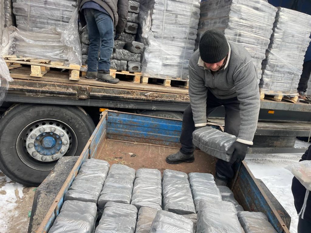 Чоловік складає паливні брикети у причіп біля вантажівки