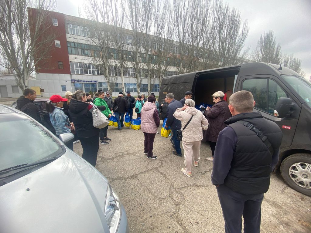 Загальний план видачі наборів біля мікроавтобуса та будівлі