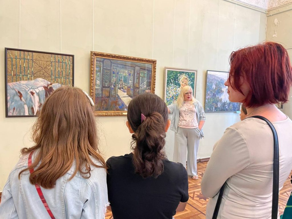 Учасники зі спини слухають екскурсоводку в залі художнього музею