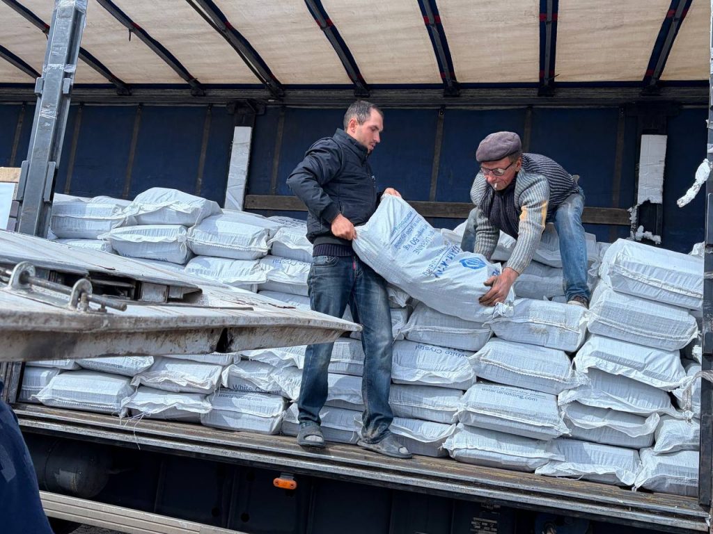 Чоловіки передають мішки паливних брикетів із відкритої вантажівки